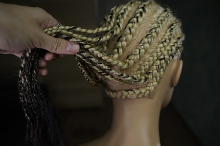 he master demonstrates to his students how to weave an African braid with Kanekalon on a mannequin,...