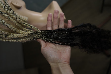 he master demonstrates to his students how to weave an African braid with Kanekalon on a mannequin, afro-locks on a frame, frame hairstyles, afro-curls, a base for hair extensions, a thin braid is braided over the head of a mannequinの写真素材