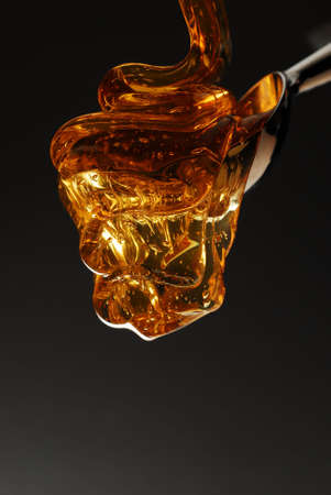 Honey pouring on spoon flowing with gold color isolated on black stock photoの写真素材