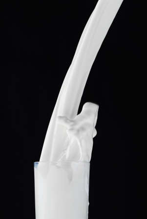Milk splashing while being poured in a glass isolated on blackの写真素材