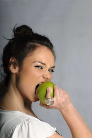 Beautiful young woman biting an apple portrait isolatedの写真素材