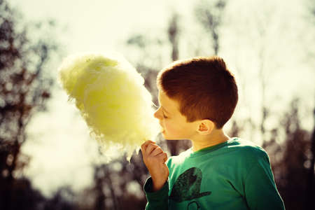 Young boy eating sugarwool in a park backlitの写真素材