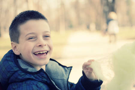 Happy young boy eating sugarwool in a parkの写真素材