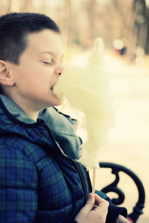 Boy bitting a sugarwool chunk in a sunny parkの写真素材