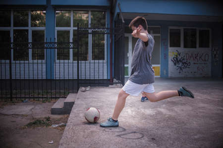 Strong kick of the ball by a young boy in the schoolyardの写真素材