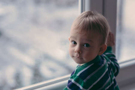 baby looking at the snow over the windowの写真素材