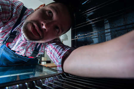 Repairman repairing the oven in the kitchen, view from inside the oven