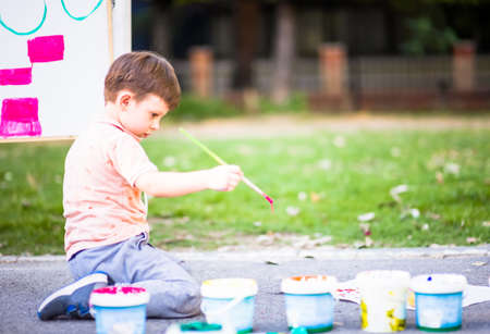 Small child playing with paintbrush on white paper into the parkの写真素材