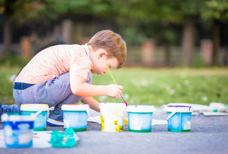 Little child sitting on the floor and holding brush for painting near the city parkの写真素材