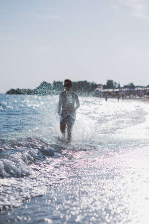 Happy kid running in the shallow water on the beach on a sunny dayの写真素材