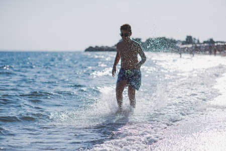 Happy kid running in the shallow water on the beach on a sunny dayの写真素材