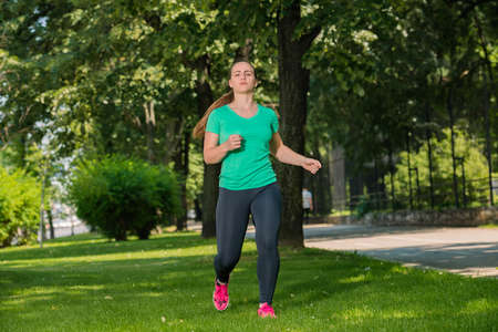 Young lady running on green lawn into the parkの写真素材