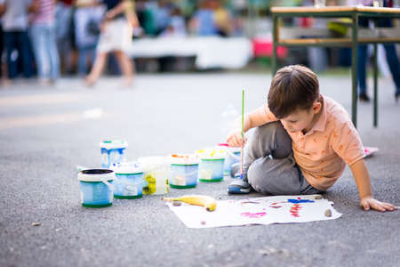 Cute boy drawing with paintbrush on paper near the parkの写真素材