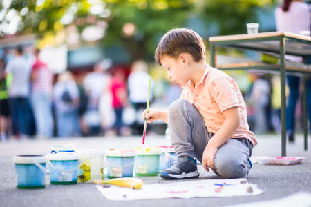 Boy sitting on the ground and holding brush for painting near the parkの写真素材