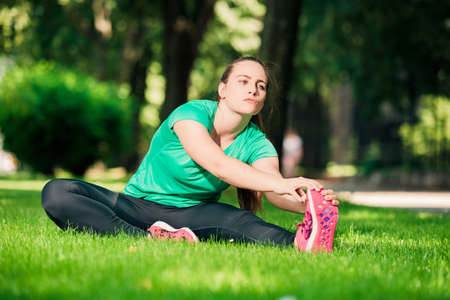 Young pretty woman sitting on the grass and stretching her legsの写真素材