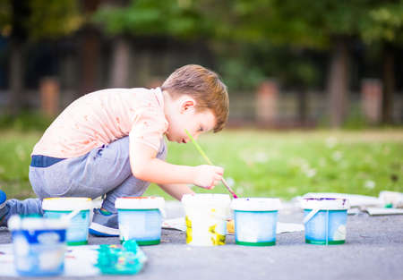 Beautiful kid holding painting brush and playing with colors near the city parkの写真素材
