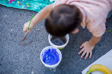Sweet child drawing on the asphalt with his paintbrush near the city parkの写真素材