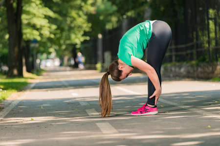 Flexible girl stretching her body on running path in the parkの写真素材