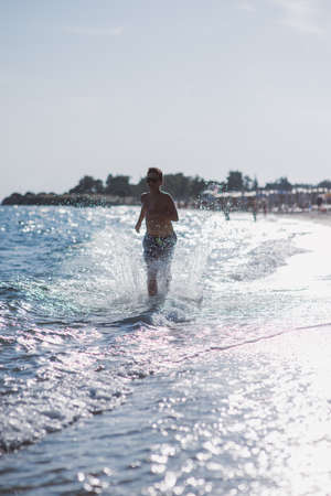 Happy kid running in the shallow water on the beach on a sunny dayの写真素材