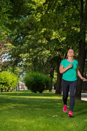 Young woman in sports wear running through the park on sunny dayの写真素材
