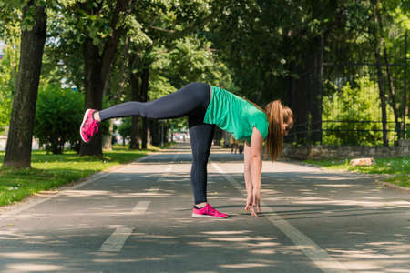 Happy young woman stretching leg muscles into the parkの写真素材