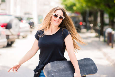 Girl with sunglasses posing with skateboard on sunny dayの写真素材