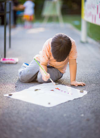 Cute boy drawing with paintbrush on paper near the parkの写真素材