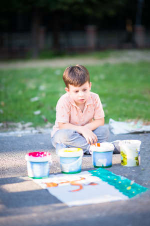 Little boy playingwith colours and painting pictures on the street near the parkの写真素材