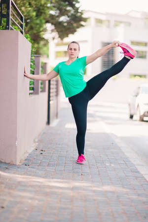 Happy young woman stretching leg muscles outdoorsの写真素材