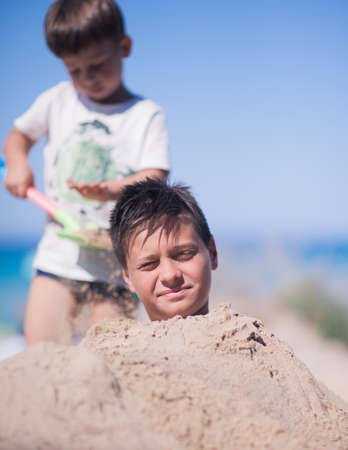 Two brothers having fun in the beach sand on a beautiful hot summer dayの写真素材