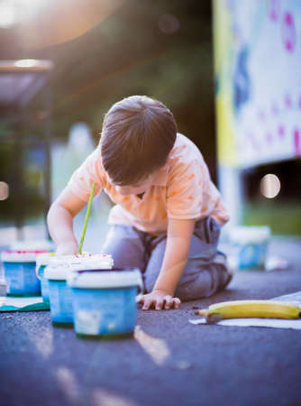 Cute boy drawing with paintbrush on paper near the parkの写真素材