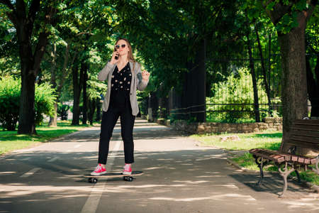 Business girl talking on smart phone in the park while driving skateboardの写真素材