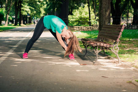 Young beautiful fitness woman stretching outdoor on the pathの写真素材