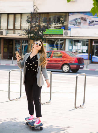 Business woman holding cellphone in the city and driving skateboardの写真素材
