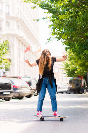 Modern Girl teenager with a skateboard at sunset on a city streetの写真素材