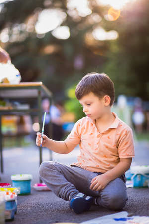 Boy sitting on the ground and holding brush for painting near the parkの写真素材
