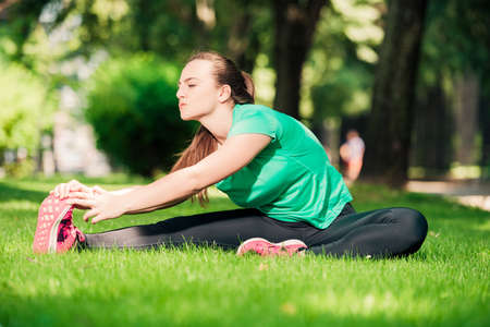 Young pretty woman sitting on the grass and stretching her legsの写真素材