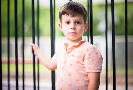 Portrait of adorable small kid standing in front of a fence near the parkの写真素材