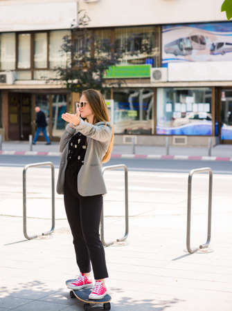 Business woman holding cellphone in the city and driving skateboardの写真素材