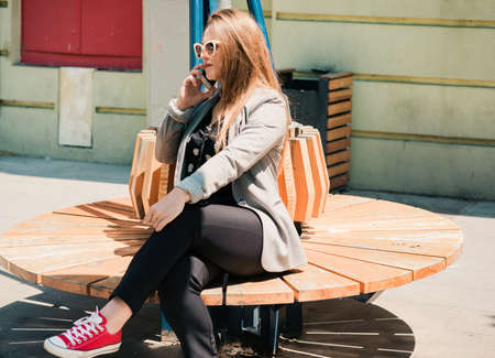 Business girl talking on cellphone while sitting on the bench on sunny dayの写真素材