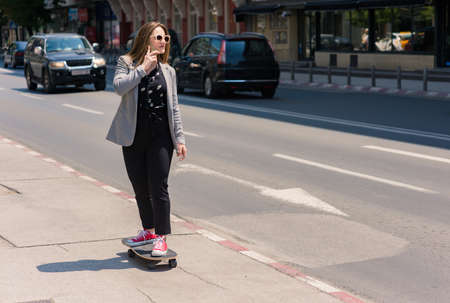 Business woman having discussion on cellphone and driving skateboard in the cityの写真素材