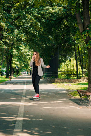 Young woman talking on cellphone with skating board on the roadの写真素材
