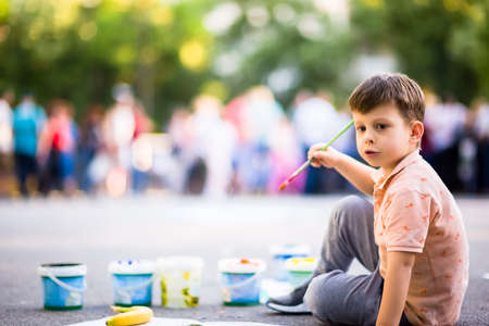 Creative child making artwork with brush and water colours on canvas near the parkの写真素材