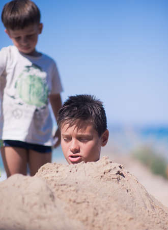 Two brothers having fun in the beach sand on a beautiful hot summer dayの写真素材