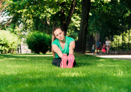 Sporty girl sitting on green lawn and doing exerciseの写真素材
