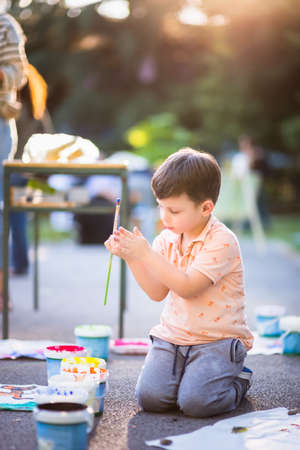 Little child sitting on the floor and holding brush for painting near the city parkの写真素材