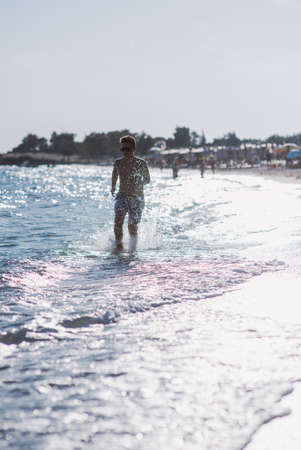 Happy kid running in the shallow water on the beach on a sunny dayの写真素材
