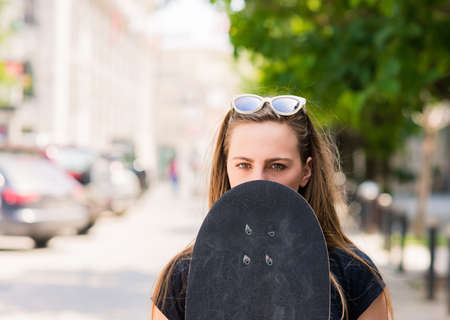 Portrait of young girl who cover her face with her skateboardの写真素材