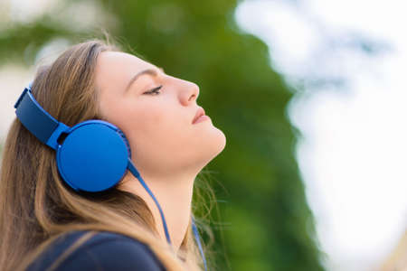 Closeup view of young girl relaxing with music on headphones in the parkの写真素材