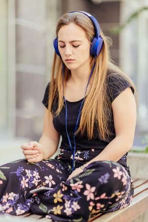 Urban portrait of a beautiful blond girl who sitting on the bench and listening musicの写真素材